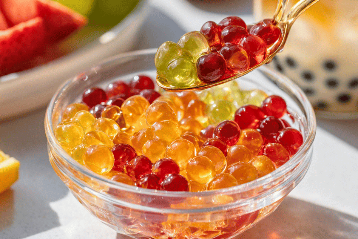 Homemade popping boba pearls made with juice and spherification, displayed in a spoon over a glass bowl.