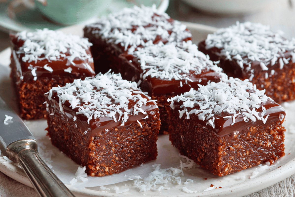 Chocolate & coconut traybake squares topped with icing and coconut on a white plate